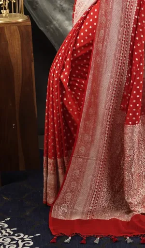 Close-up of Handwoven Pure Khadi Georgette Banarasi saree in red, featuring white polka dots and a beautifully detailed gold zari border with floral motifs. The saree is finished with elegant tassels at the edge, adding a traditional touch to the design.