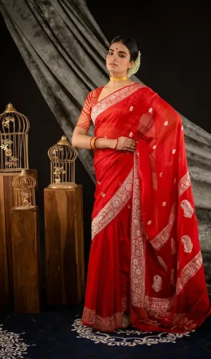 Model wearing a Handwoven Pure Khadi Georgette Banarasi saree in vibrant red, featuring intricate white floral embroidery and paisley motifs along the border. The saree is elegantly draped, showcasing traditional craftsmanship in a luxurious setting.