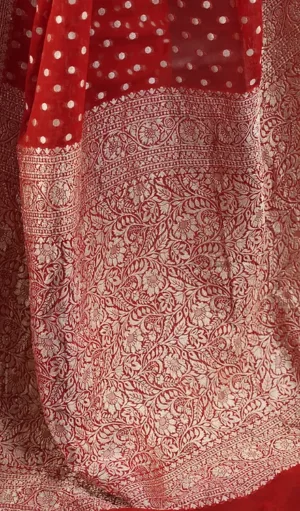 Close-up of Handwoven Pure Khadi Georgette Banarasi saree in red, featuring white polka dots and an intricate gold zari border with floral and paisley motifs. The elegant design highlights the traditional craftsmanship and luxurious appeal of the saree