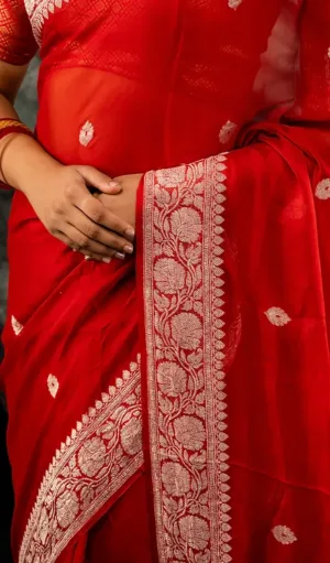 Close-up of a woman wearing a red Handwoven saree with intricate white floral embroidery along the border. The saree features delicate floral motifs scattered across the fabric, offering a graceful and traditional look.