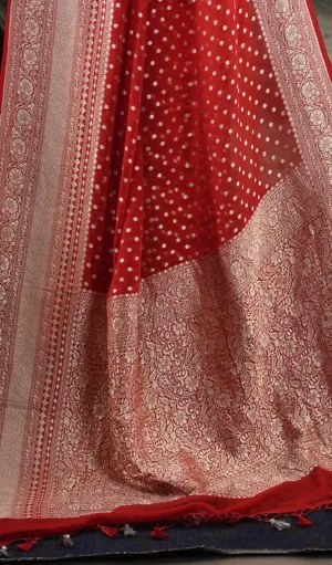 Close-up of Handwoven Pure Khadi Georgette Banarasi saree in red, featuring delicate white polka dots and an intricate gold zari border with floral motifs. The pallu gracefully drapes, showcasing traditional craftsmanship and modern elegance.