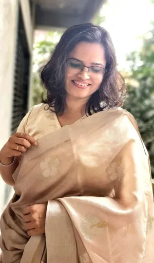 Woman wearing a beige handloom silk Chanderi saree with floral patterns, smiling while adjusting her saree.