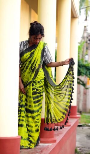 Woman wearing a green and black tie-dye saree with tassels, standing gracefully and holding the pallu, showcasing traditional attire.