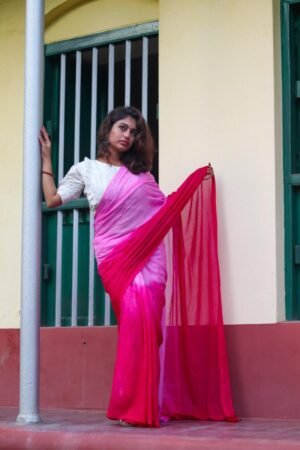 A woman draped in a handwoven mul cotton saree featuring shades of pink, standing against a wall with green windows.