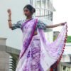 A woman wearing a purple mul cotton tie-dye saree with a contrasting border and tassels, posed gracefully outdoors.